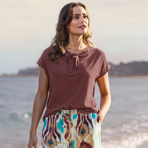 Frauenmodel trägt T-Shirt, Braun, Kurzarm, Rundhals mit Schleifendetail, gemusterte Hose, Vorderansicht