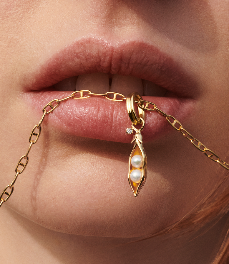 Close up of a model biting a necklace chain with a pea pod charm
