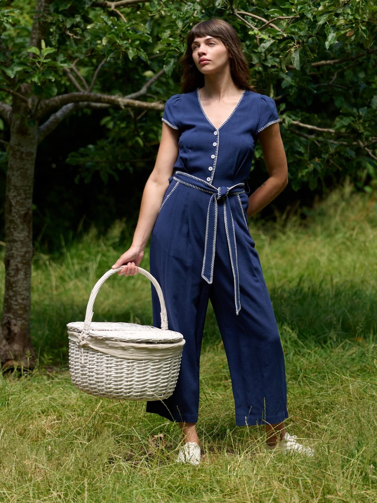 Image of the model wearing navy marleen blanket stitch jumpsuit in the woods.