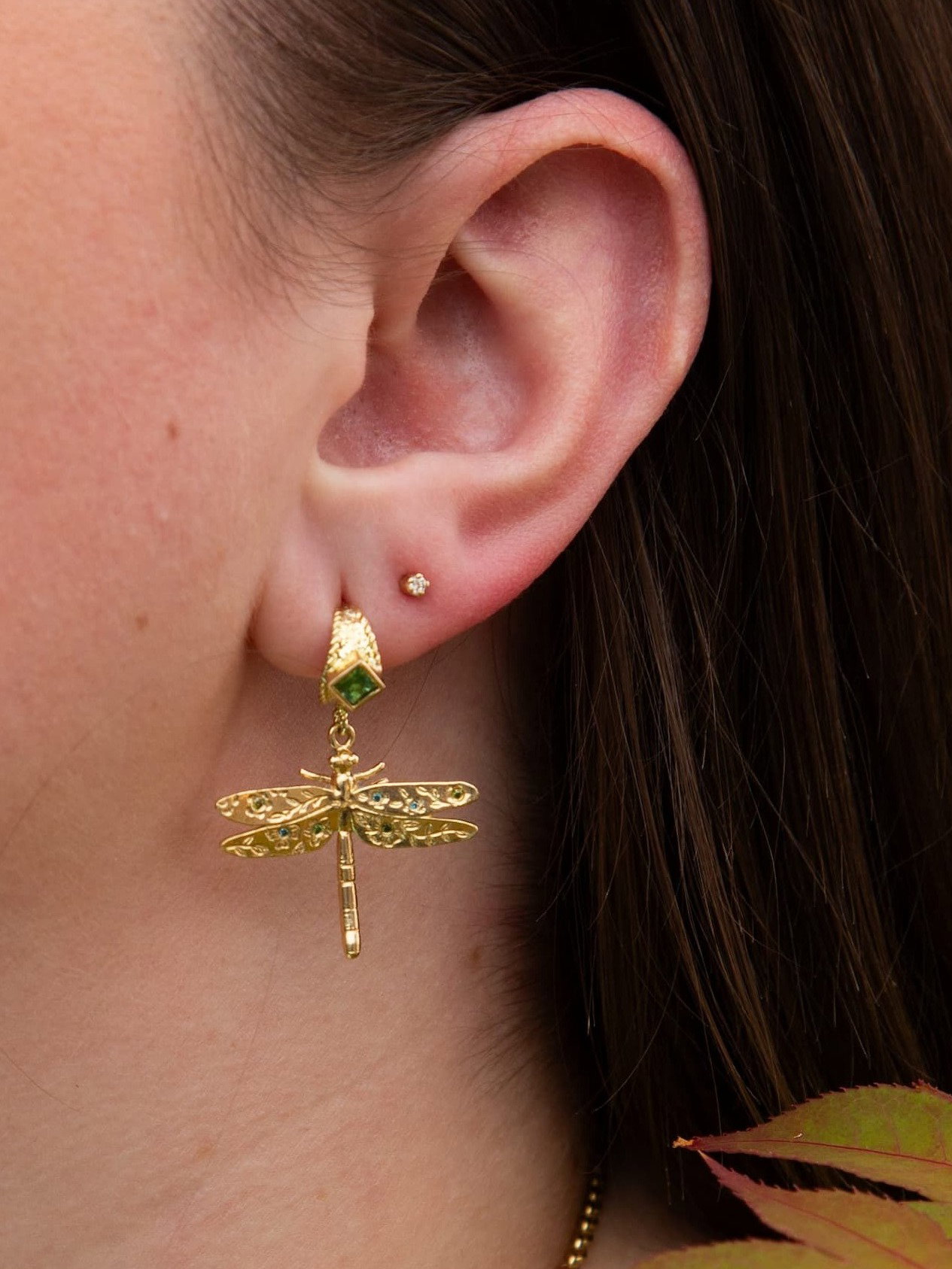 Close-up of the Floral Engraved Dragonfly Drop Huggie Hoop Earring with Tourmalines and Blue & Green Diamonds, featuring a gold dragonfly drop suspended from a huggie hoop set with a green tourmaline, worn on the ear.