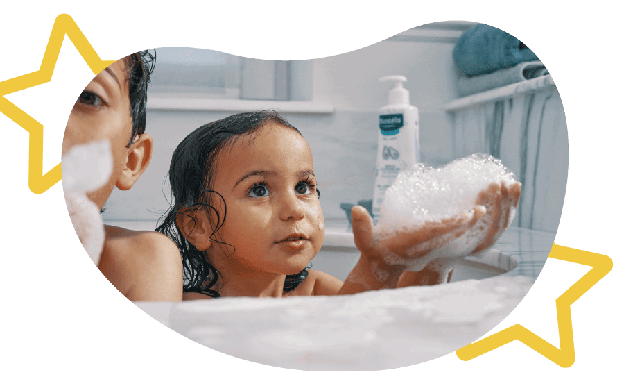 A brother and sister blowing bubbles with a Mustela product in the background