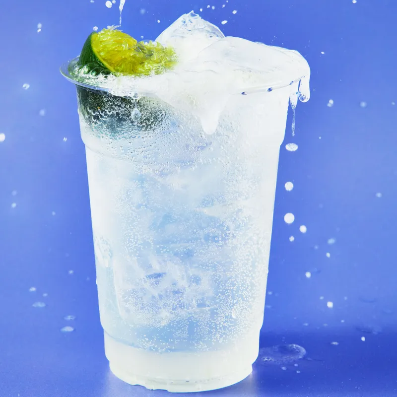 A gin and tonic in a plastic cup with half a squeezed lime.