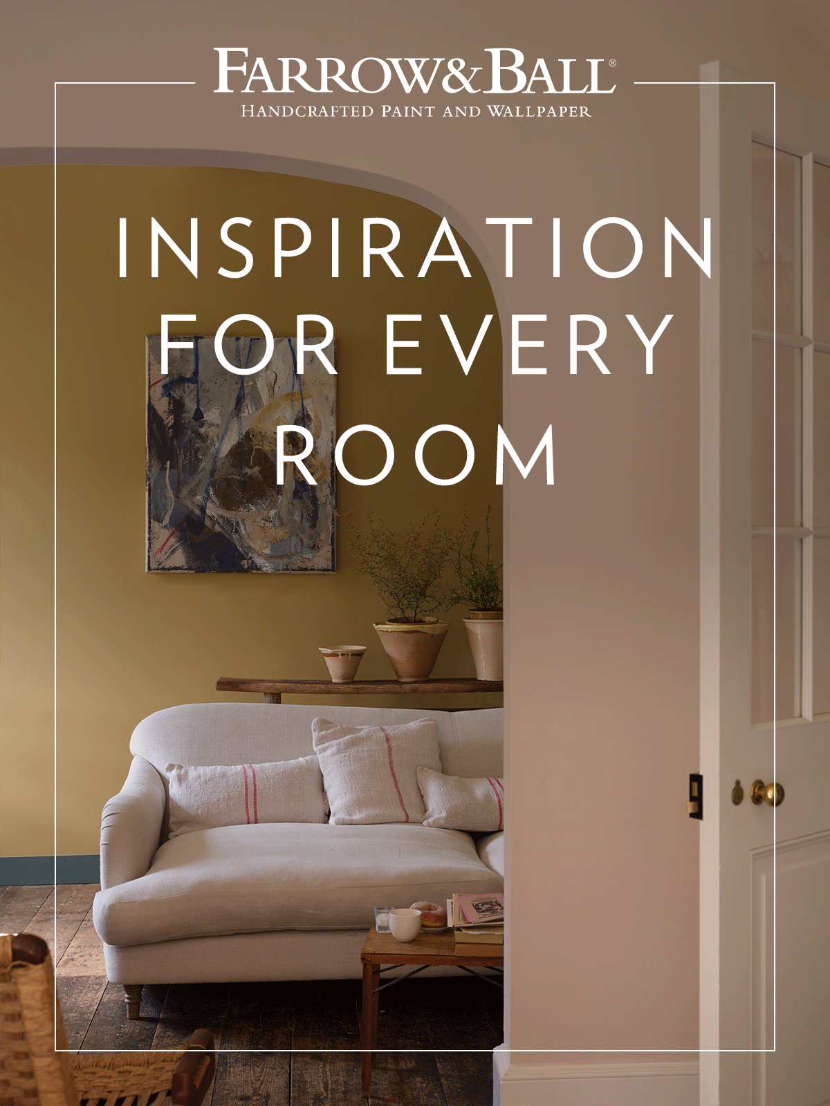 An interior view through a pale pink arched doorway looking into a room with an ochre yellow feature wall. The space features a light grey sofa, an abstract painting, and rustic terracotta pots on a wooden shelf over dark floorboards.
