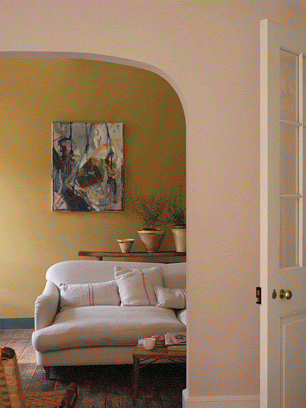 A GIF showing two scenes: first, a small cobblestone courtyard with green-painted brick walls, potted plants, and sculptural stone tables beside steps leading to a tall glass door; then a cosy living room with a mustard-yellow wall, light sofa with striped cushions, abstract artwork, and plants on a wooden console table.