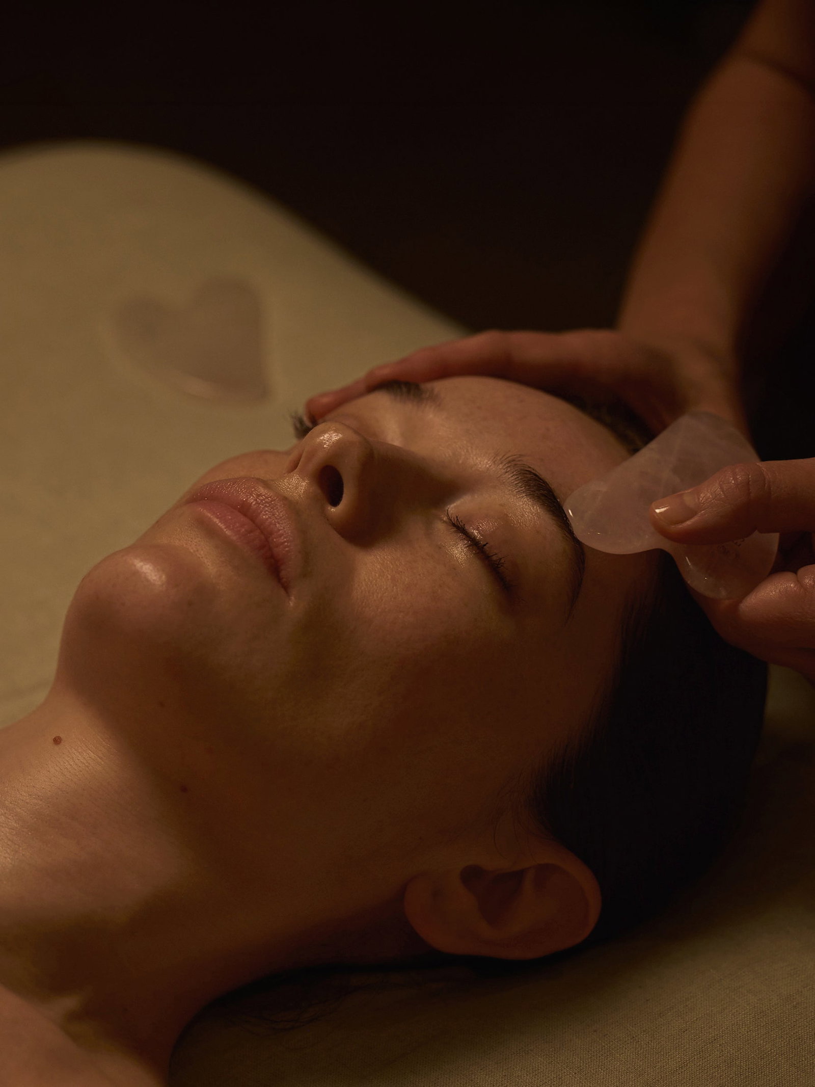 Model laid on therapist bed with therapist applying guq sha to temple