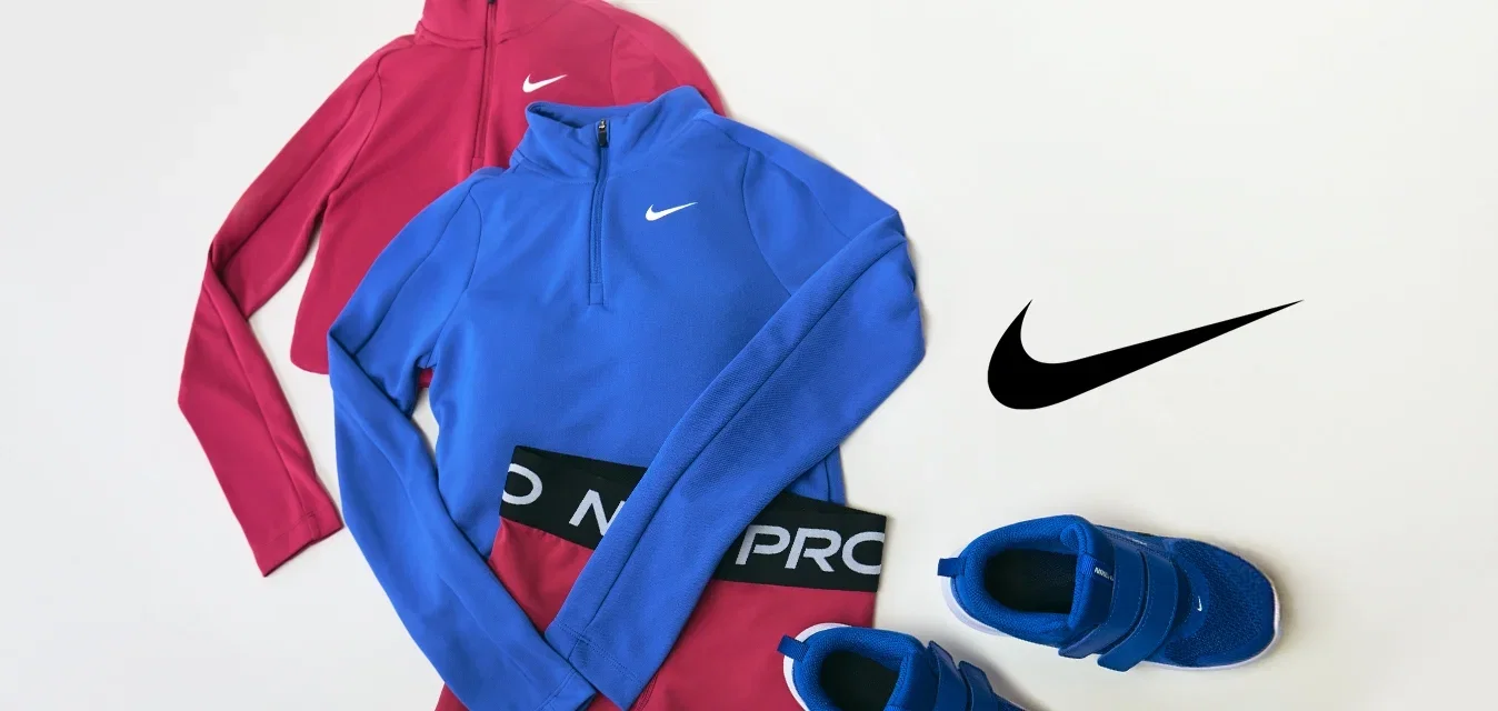 Completo sportivo Nike rosso e blu costituito da due maglie con mezza cerniera, leggings coordinati e un paio di scarpe da ginnastica blu su sfondo bianco.