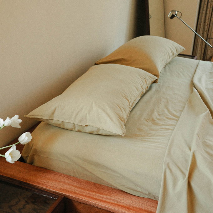Light green sheets on a wooden bed frame next to white flowers