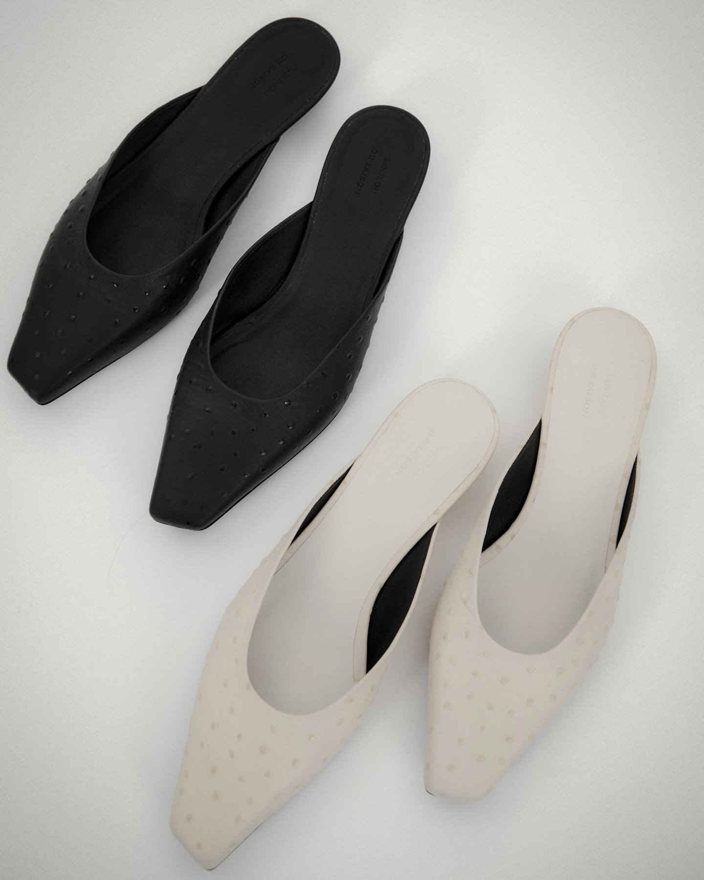 Flatlay of two pairs of women's pointed-toe slip-on mules — one black and one cream with dotted texture on a light background