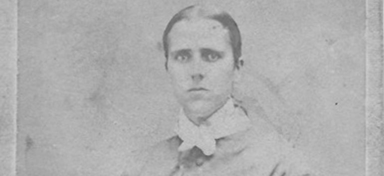 Black-and-white portrait of a young person with short hair, wearing a high-collared shirt and jacket, with a serious expression against a plain background.