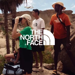 Groupe de quatre personnes à l'extérieur : l'une utilise des jumelles, portant une chemise verte et un short noir. Les autres sont en t-shirts et shorts. L'arrière-plan présente des rochers et de la végétation.