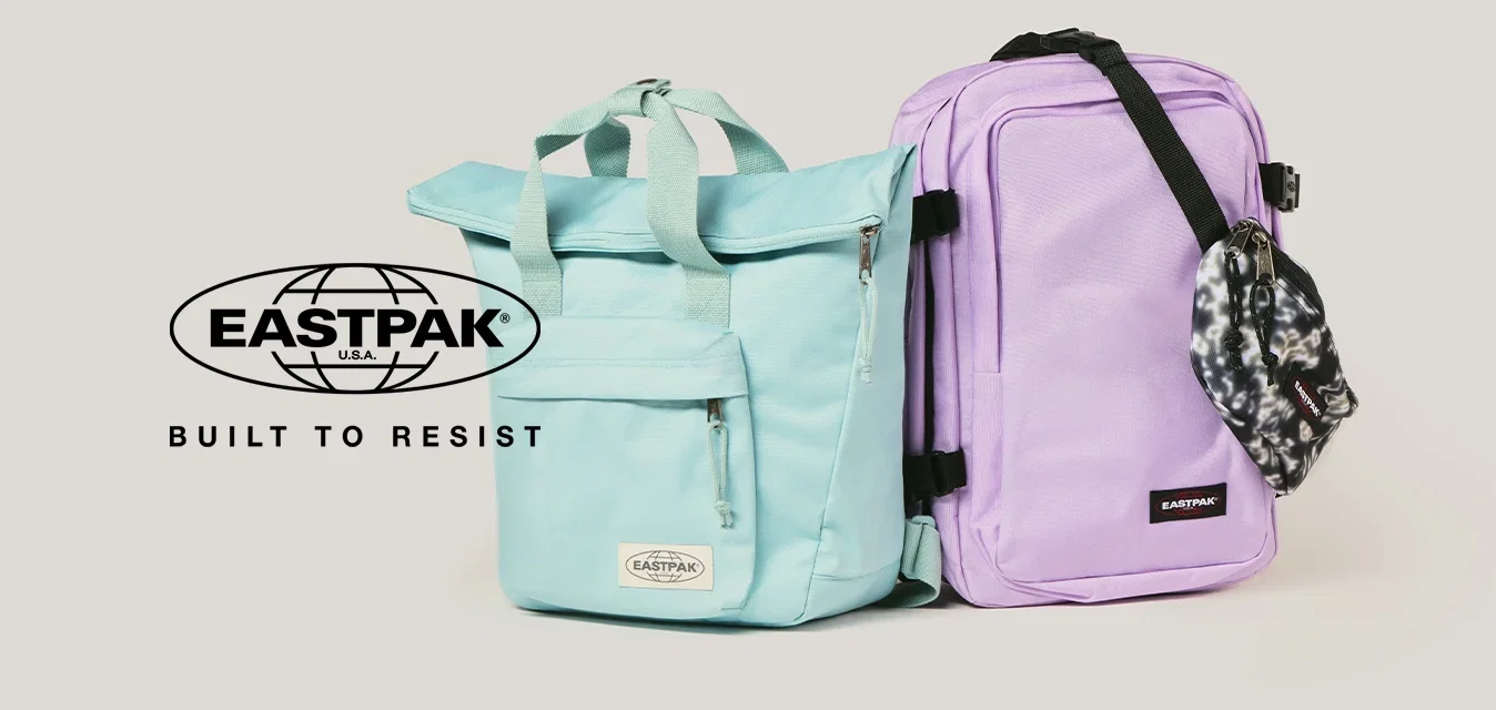Deux sacs à dos Eastpak côte à côte, l'un bleu clair avec des poignées, l'autre lavande avec une sangle noire et une poche à motifs accrochée, sur un fond neutre.