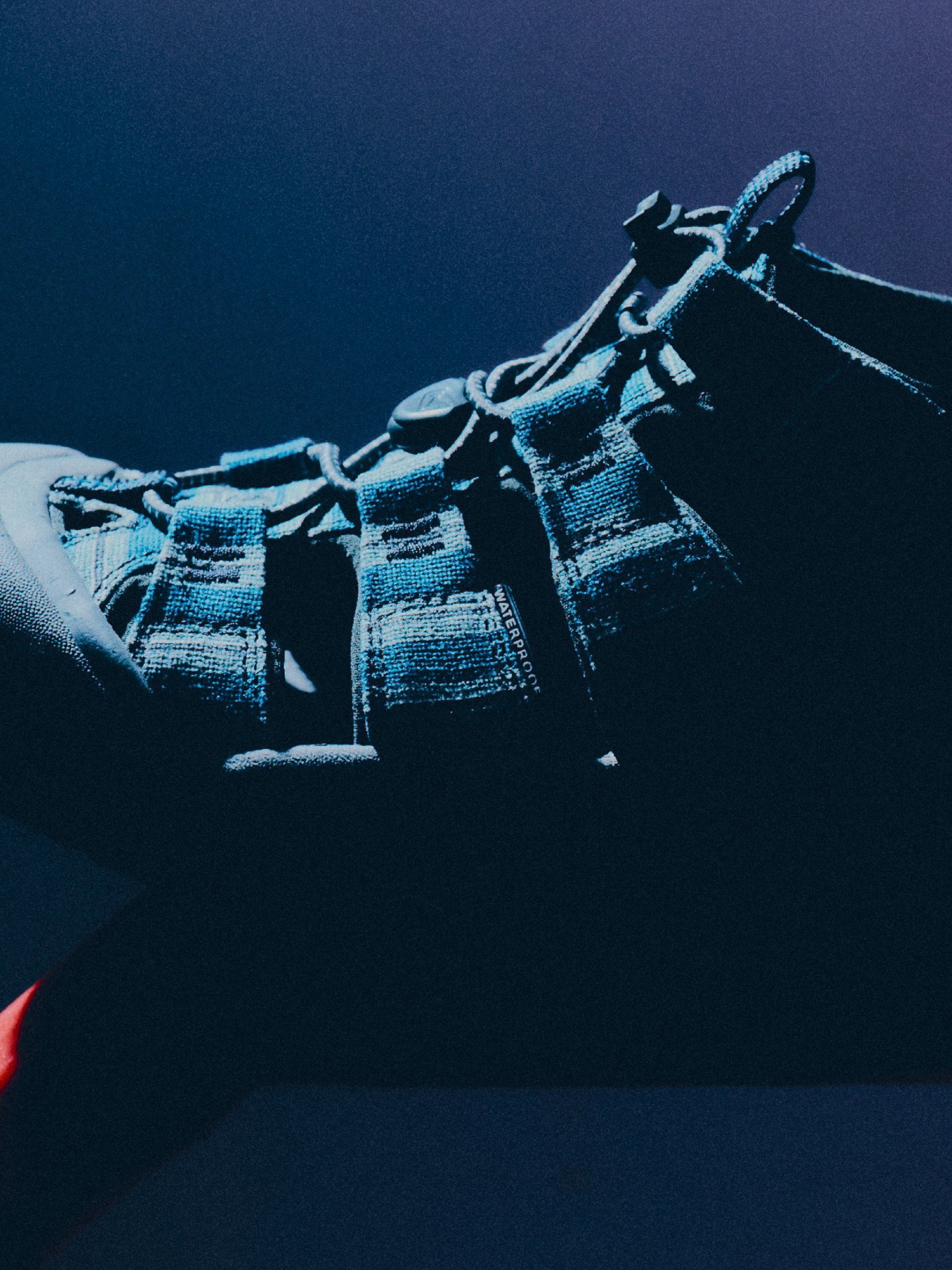 Close-up of a dark blue strappy outdoor sandal with adjustable buckle, textured webbing straps and rugged sole, in moody low-key lighting