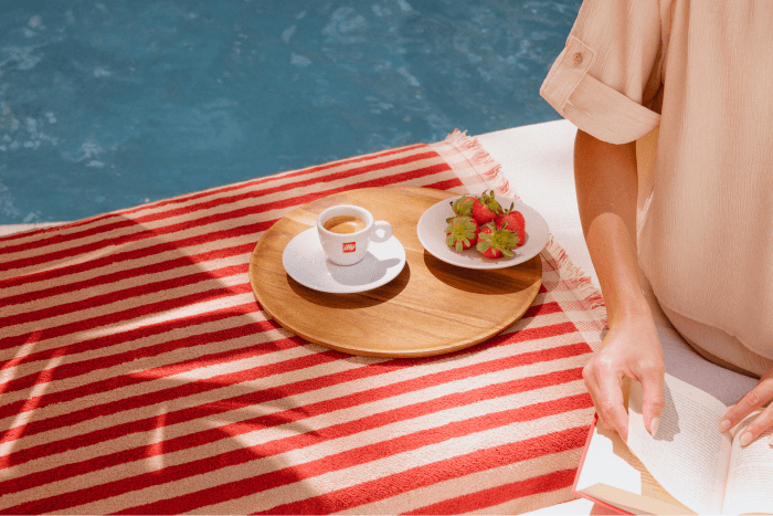 Person relaxing poolside with an espresso, fresh strawberries, and an open book