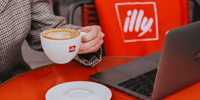Person enjoying a cup of illy coffee while working on a laptop