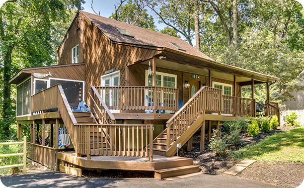 Wood-sided house with wraparound deck, stairs, and trees surrounding the property.