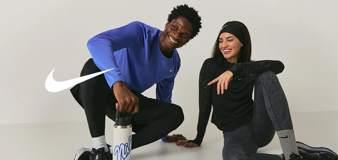 Dos personas con ropa deportiva sentadas en el suelo, sonriendo; una sostiene una botella de agua, ambas parecen relajadas y amistosas.