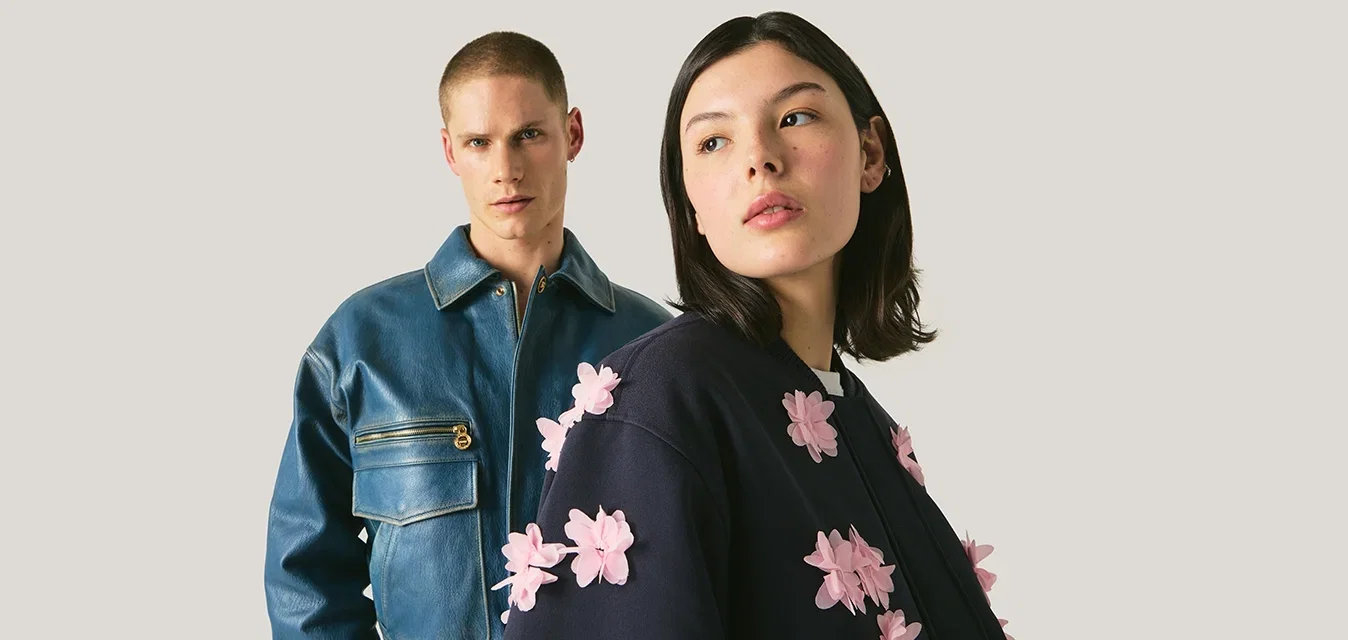 Dos modelos que llevan chaquetas de moda, uno con una chaqueta de cuero azul y el otro con una chaqueta azul marino con apliques florales rosas en relieve.