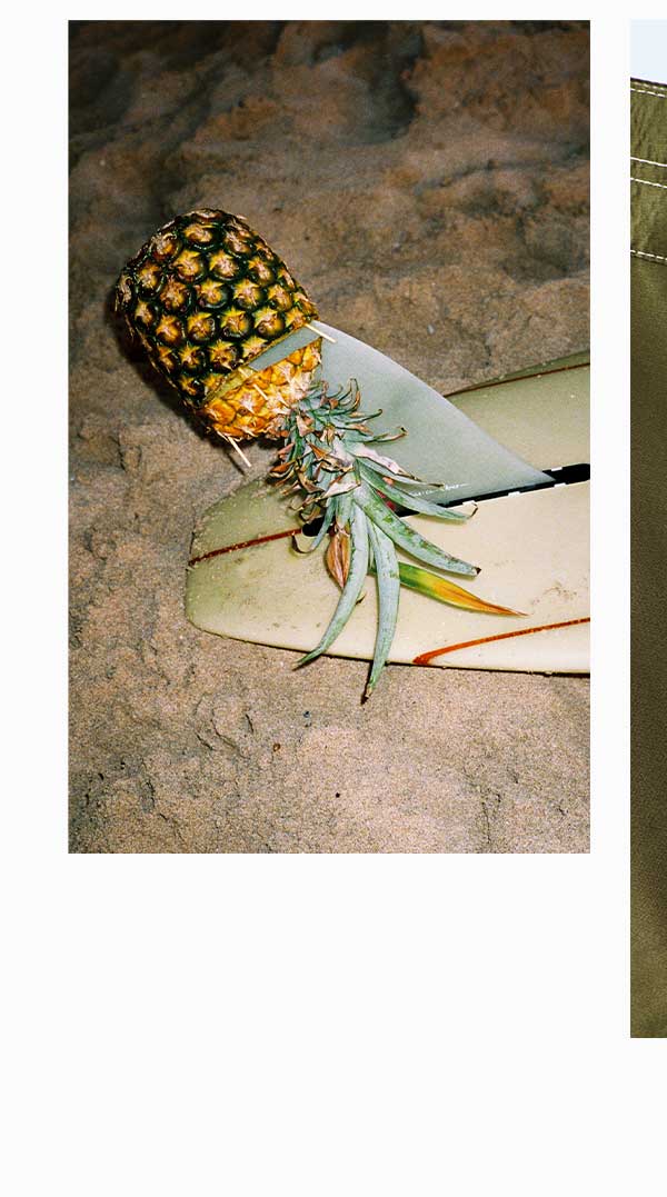 A pineapple drink resting on a surfboard fin