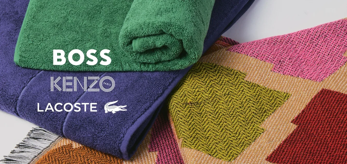 Pile de serviettes pliées, une verte enroulée, une violette pliée, posées sur un tapis coloré à motifs géométriques avec des bords frangés.