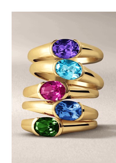 A stack of five gold rings featuring oval cut gemstones in vibrant jewel tones.