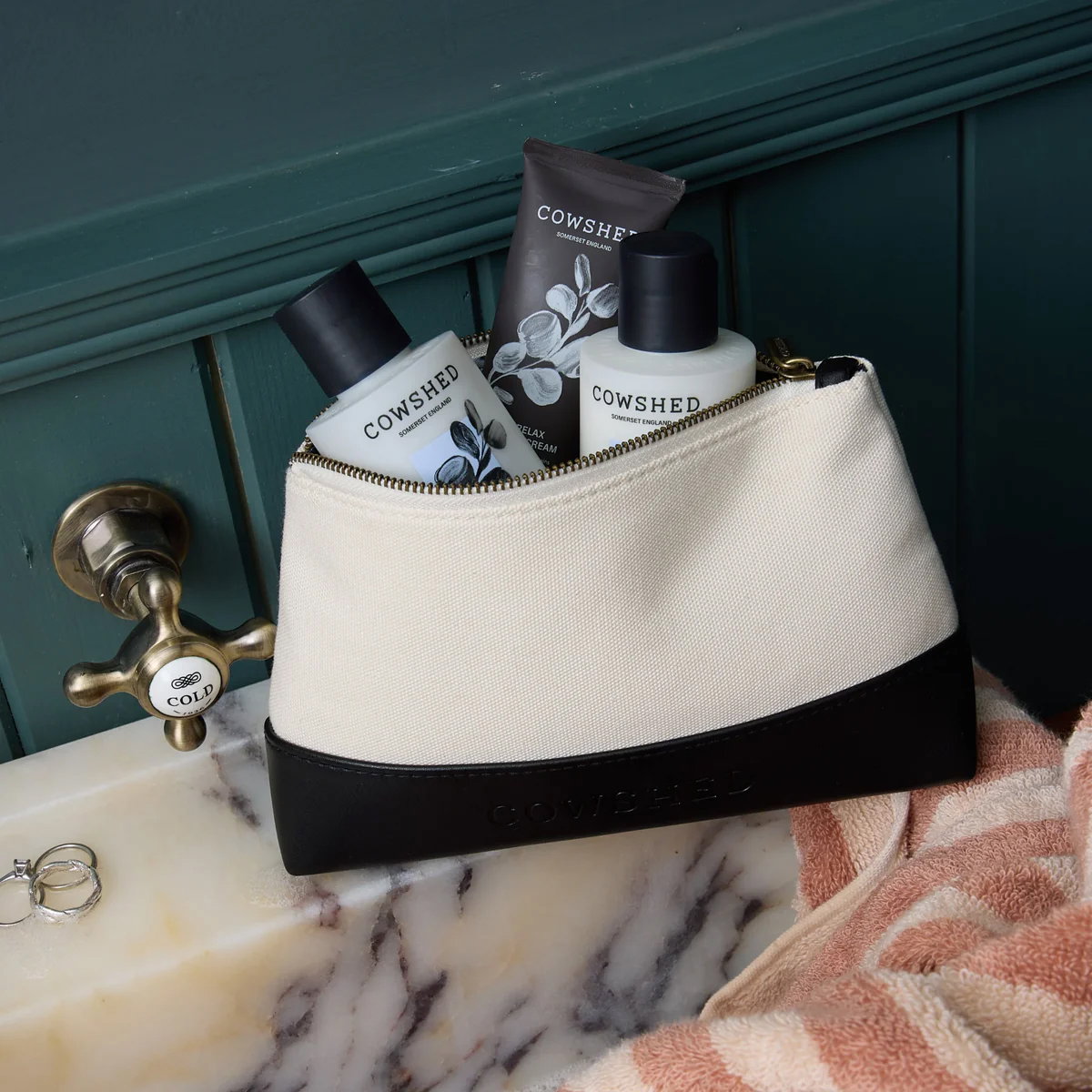 A travel wash bag full of Cowshed products at a marble sink