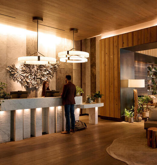 A man checks in at a hotel reception desk with warm wooden decor and soft lighting. 