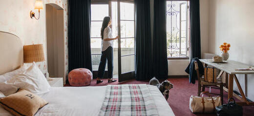 A woman looks out onto the balcony of her modern hotel room. 