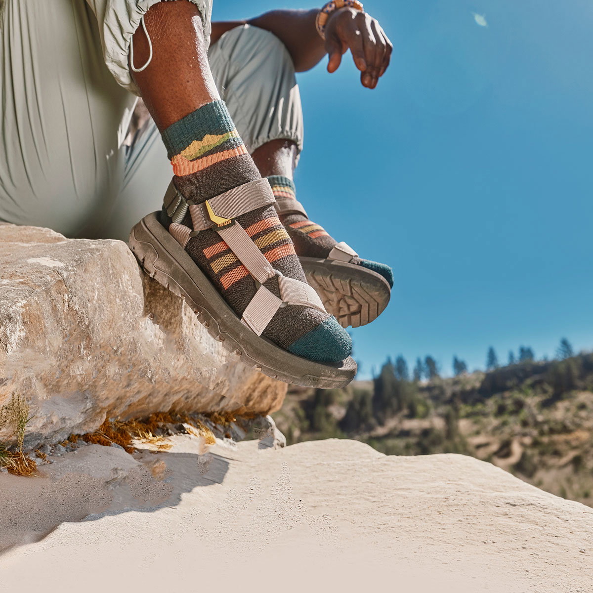 A person sat on the edge of a rocky surface, wearing Teva sandals.