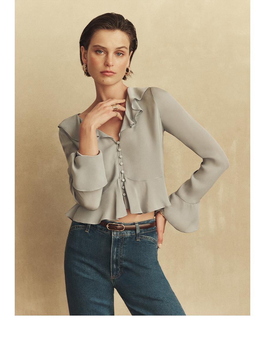 An image of a woman wearing a light blue blouse and medium blue denim jeans.