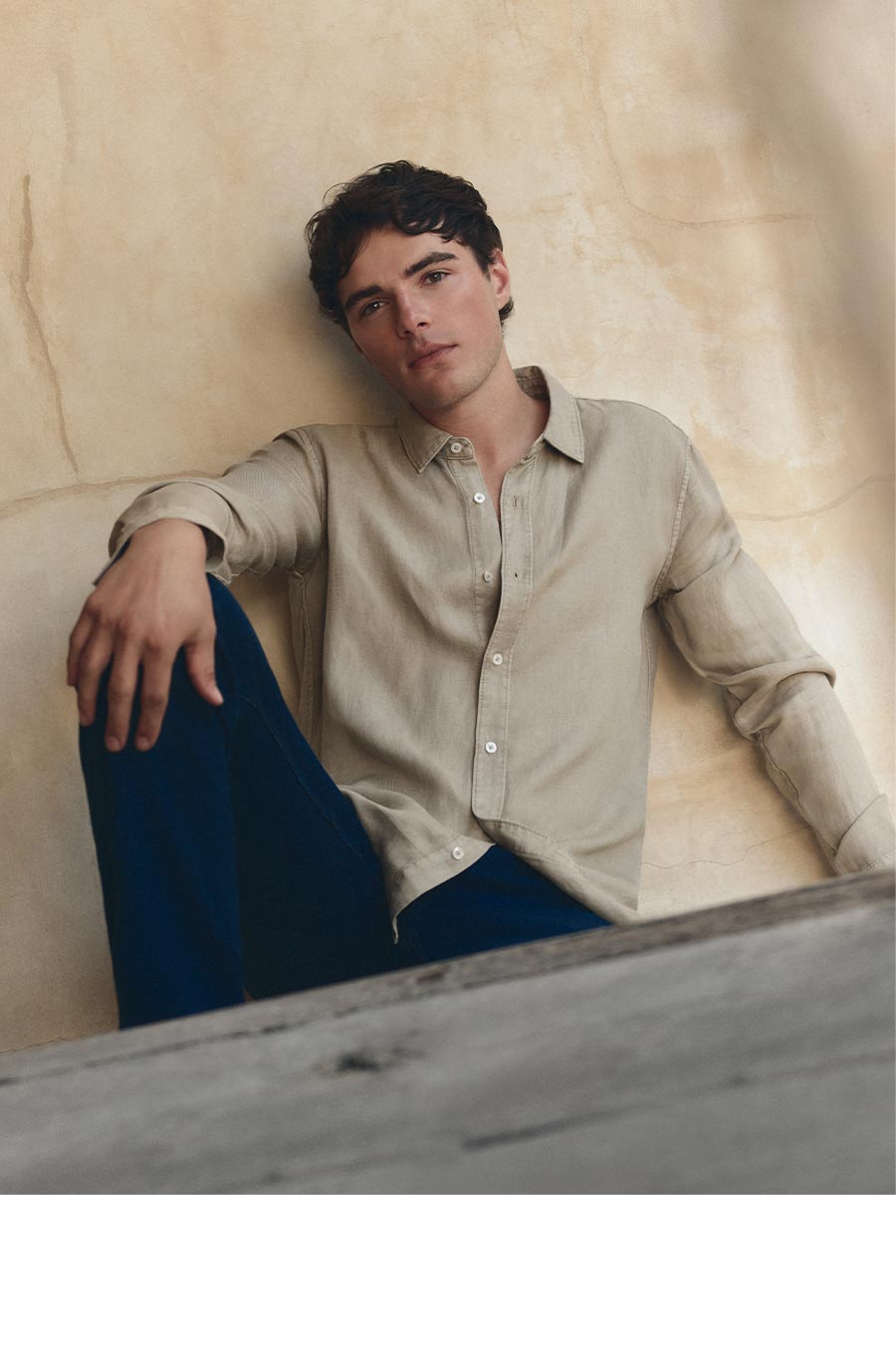A man wearing a beige shirt and blue jeans.