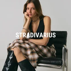 Giovane donna che indossa un top senza maniche nero, una gonna scozzese e stivali neri alti, seduta su una moderna sedia in pelle nera.