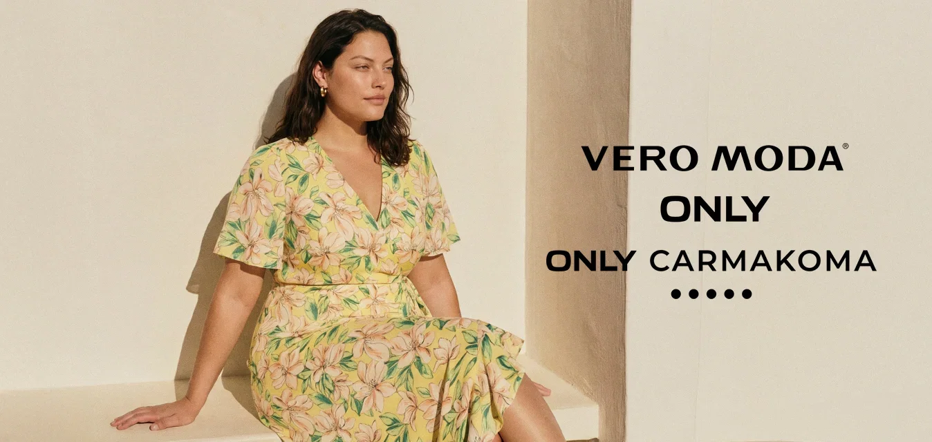 Donna con capelli scuri seduta su una panchina bianca, indossa un vestito giallo a fiori e sandali neri con tacco sotto una luce naturale intensa.