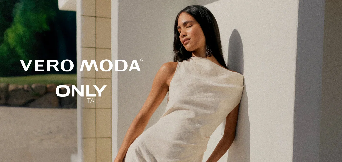 Donna con un vestito bianco senza maniche appoggiata a un muro bianco all'aperto, occhi chiusi, con la luce del sole che proietta ombre sulla sua figura.
