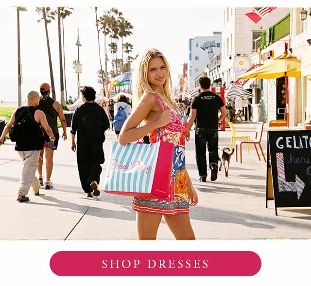 Model wearing a multi tile print dress holding a shopping bag. Shop dresses. 