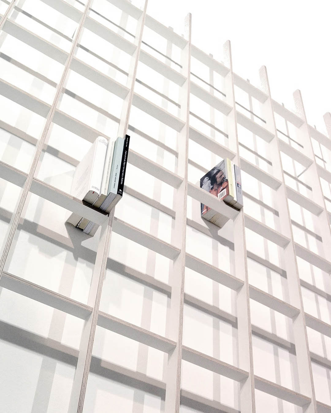 Minimalist wall-mounted wooden grid bookshelf with a few books tucked into square compartments against a white wall
