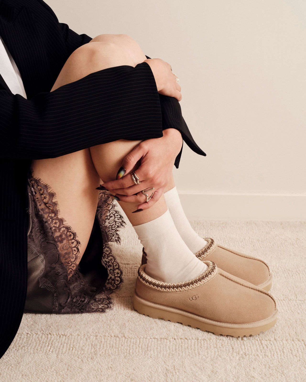 Person sitting, wearing black top, lace shorts, white socks, and Tasman II Slipper.