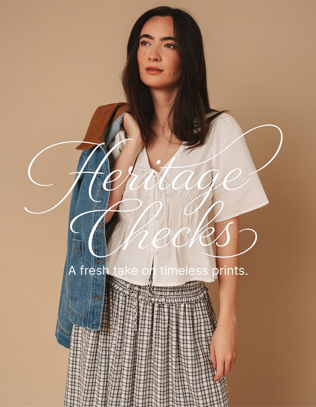 Model wears a white blouse, check skirt, and denim jacket. Text: “Heritage Checks.”