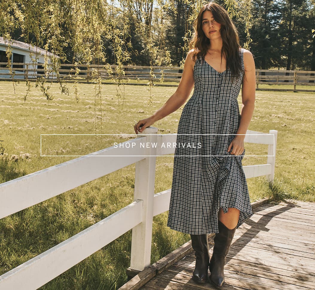 Model wears a navy check midi dress with black knee-high boots outdoors. “Shop New Arrivals.”