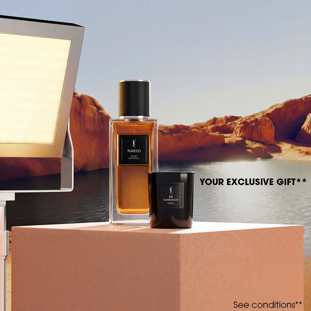 A bottle of YSL "Le Vestiaire des Parfums" and a black scented candle displayed on a stone pedestal in front of a canyon lake.