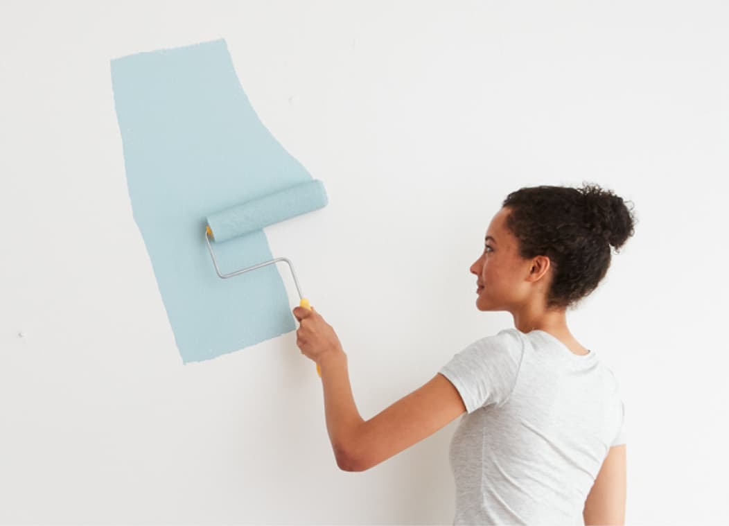 Woman rolling blue paint on the wall with paint roller