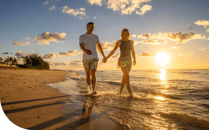A couple strolls along a Caribbean beach at sunset.
