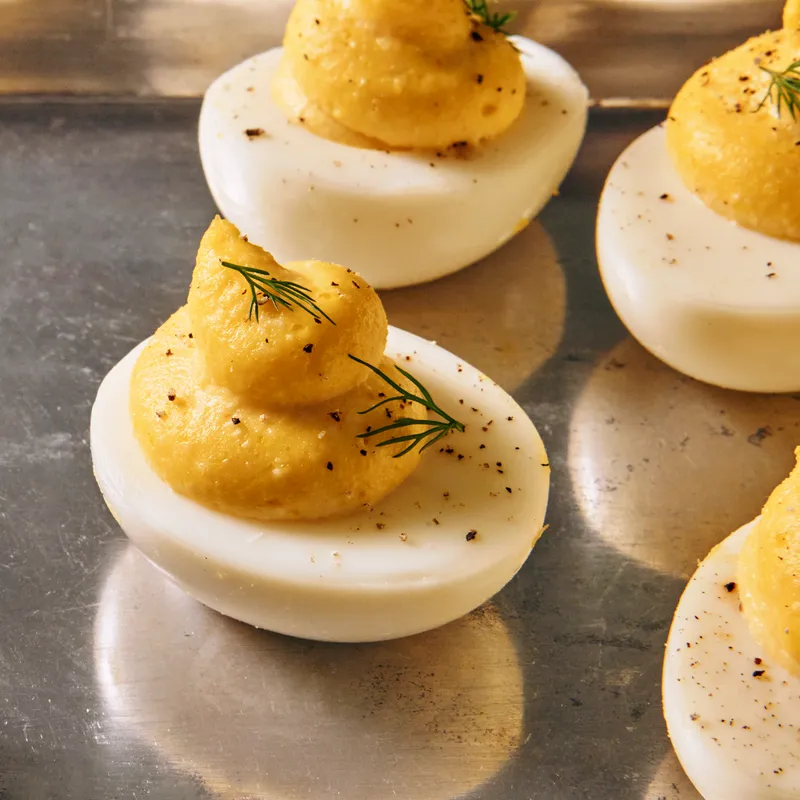A multitude of deviled eggs, garnished generously with pepper and dill sprigs, on a reflective silver platter.