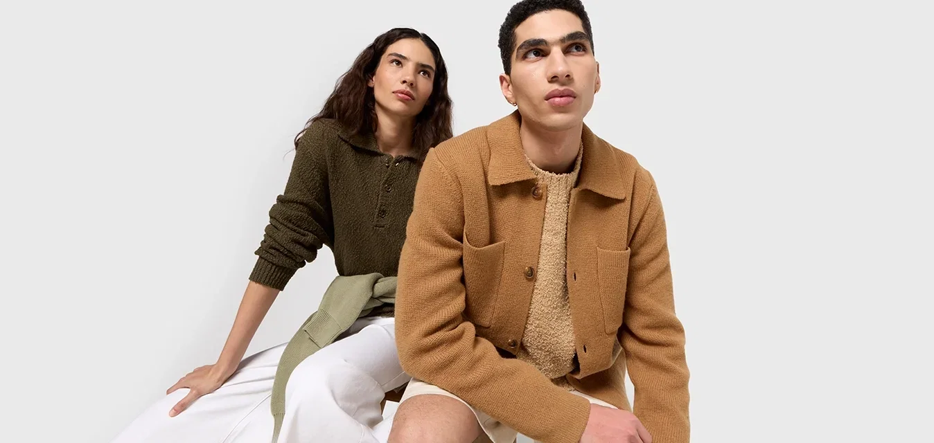 Twee modellen zitten zij aan zij. De vrouw draagt een donkergroen gestructureerd sweater; de man heeft een lichtbruine gestructureerde shirtjas over een crèmekleurig top.