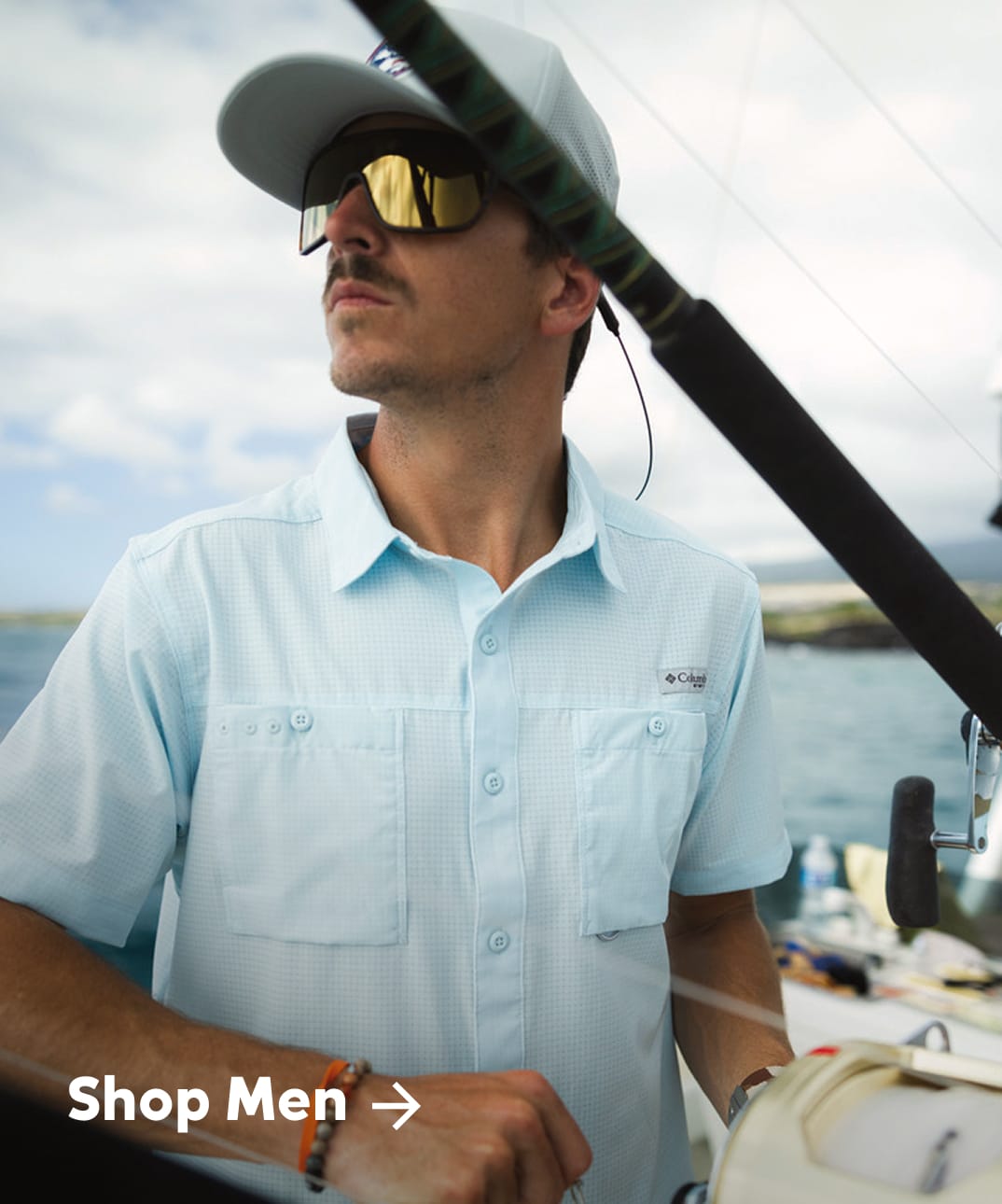 A man wearing a light blue button-up top on a boat with text: Shop Men