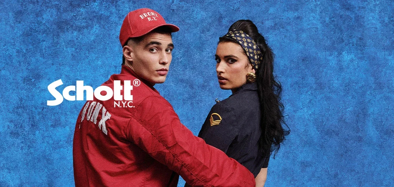 Jeune homme en veste rouge Bronx et casquette, tenant la taille d’une femme en combinaison sombre et bandeau à motifs, devant un fond texturé bleu.