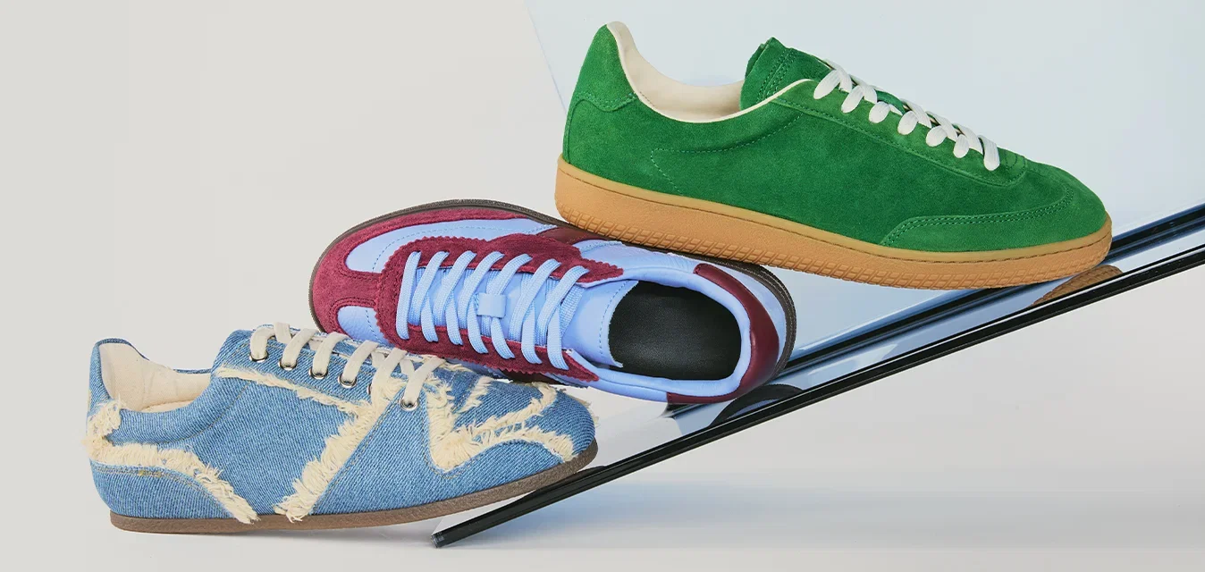 Trois baskets colorées en bleu, rouge et vert équilibrent sur une tige métallique noire inclinée sur un fond clair.