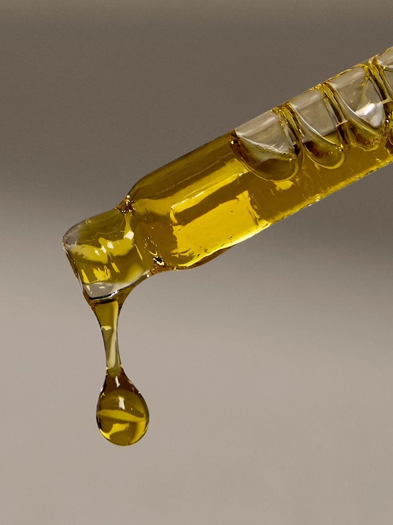 close up of pipette with oil dripping out with one droplet falling and bubbles in the oil/pipette