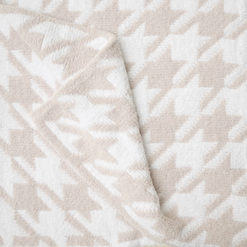 Close-up of a plush Kashwére throw featuring a large houndstooth pattern in soft cream and beige with the corner folded to reveal its luxurious texture.