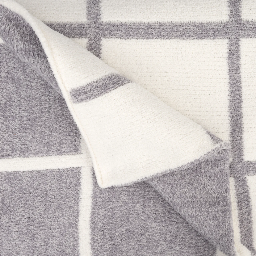 Close-up of a reversible Kashwére throw featuring a cream and soapstone windowpane pattern with the corner folded back to reveal the reverse side.