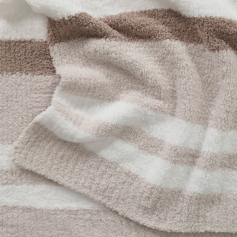 Close-up of a plush Kashwére throw with wide horizontal stripes in mink, bone, and white, emphasizing its soft texture and layered folds.